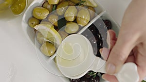 Pouring olive oil, over olive salad with green and black olives and lemon, top view