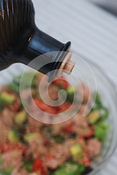 Pouring Olive Oil over Spoon in Aurugula Salad with Tomatoes and Avocado. Healthy Food concept.