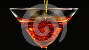 Pouring orange cocktail in martini glass on black background