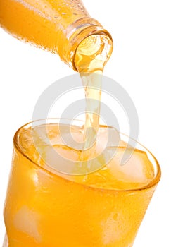 Pouring orange soda into glass with ice from bottle
