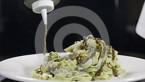 Pouring pesto sauce into plate with cooked pasta on black background. Slow motion. Cooking delicious meal. Italian