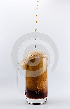 Pouring process of dark stout beer into a beer glass mug, splashes, drops and froth around glass mug