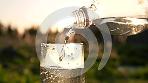 Pouring Pure Mineral Drinking Water From Bottle Into Glass Against Sunset Shines