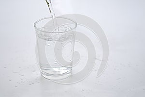 Pouring pure water into a glass on wood with wite background.