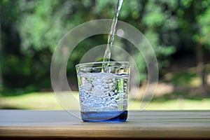 Pouring pure water in to the glass make spread of water crystal bubble with grass field background
