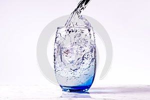 Pouring purified drinking water into a blue glass, white background carrara marble base. full glass