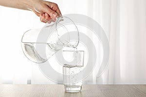 Pouring purified fresh water from the jug in glass on table