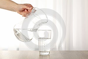 Pouring purified fresh water from the jug in glass on table