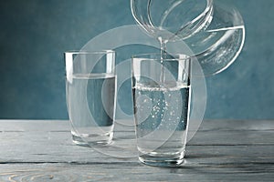 Pouring purified fresh water from the jug in glass on table