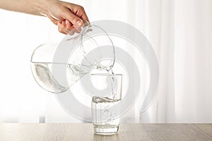 Pouring purified fresh water from the jug in glass on table