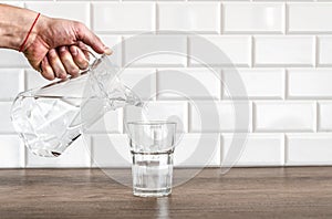 Pouring purified fresh water from the jug in glass on table