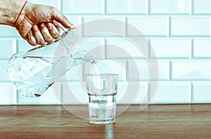 Pouring purified fresh water from the jug in glass on table