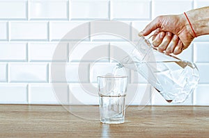 Pouring purified fresh water from the jug in glass on wooden table