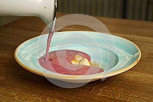 Pouring raspberry cream soup into a bowl on a wooden table