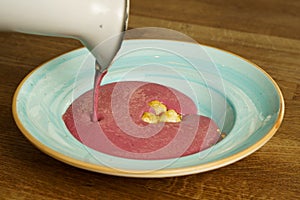 Pouring raspberry cream soup into a bowl on a wooden table