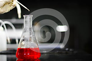 Pouring a red chemical on a glass conical flask with a dropper in a chemistry lab