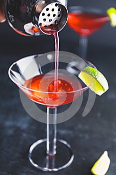 Pouring red cocktail with lime in Martini