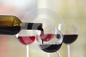 Pouring red wine from bottle into glass on blurred background, closeup