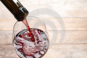 Pouring red wine from bottle into glass on blurred background