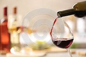 Pouring red wine from bottle into glass on blurred background.