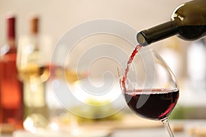 Pouring red wine from bottle into glass on blurred background photo