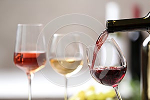 Pouring red wine from bottle into glass on blurred background