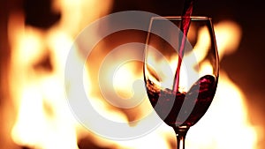 Pouring red wine into a glass against the background of fire in the fireplace