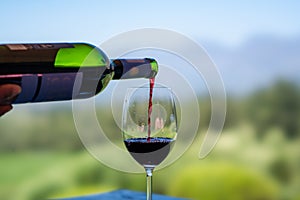Pouring red wine into the glass against nature blurred background