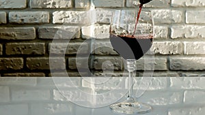 Pouring red wine into a glass on a brick wall background,close-up