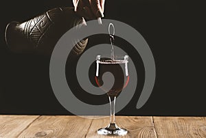 pouring red wine into a glass from a clay bottle on a black background