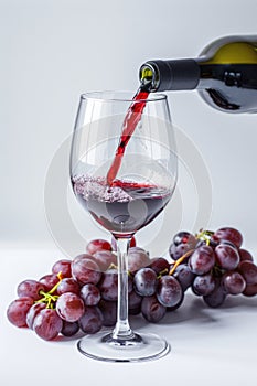 Pouring red wine into glass, grapes around, isolated on white background. AI Generated