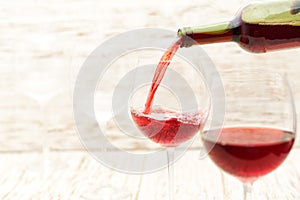 Pouring red wine into the glasses against  white wooden background photo