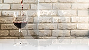 Pouring red wine into a wine glass against a white brick wall background,a beautiful glass with wine,an alcoholic drink.