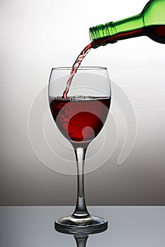 Pouring red wine into the wineglass close-up, isolated on light gradient background