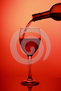 Pouring red wine into the wineglass close-up, isolated on pink gradient background