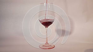 Pouring red wine into wineglass, white background.