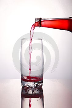 Pouring a refreshing red bubbly soda drink from bottle into glass on white background closeup with reflections
