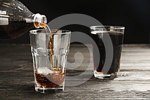 Pouring refreshing soda drink into glass on black wooden table against dark background