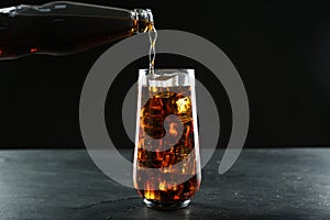 Pouring refreshing soda water from bottle into glass on black table