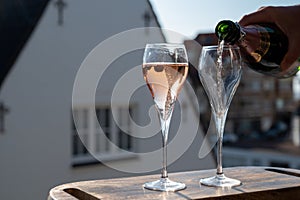 Pouring of rose champagne sparkling wine in flute glasses on outdoor terrace in France