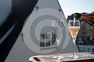 Pouring of rose champagne sparkling wine in flute glasses on outdoor terrace in France