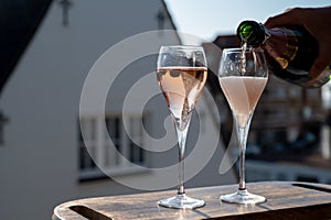 Pouring of rose champagne sparkling wine in flute glasses on outdoor terrace in France