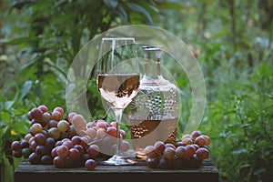 Pouring rose wine from a bottle into glass on table with pink grapes