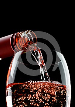 Pouring rose wine from bottle to glass on black