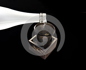 Pouring sake from bottle into Bizen-yaki or Bizen ware cup and square box on black background photo