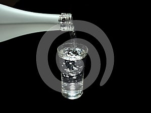 Pouring sake, liquor made from rice, from sake bottle into a shot glass on black background