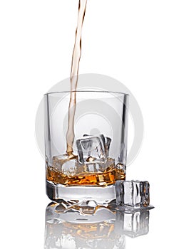 Pouring scotch whiskey in glass with ice cube