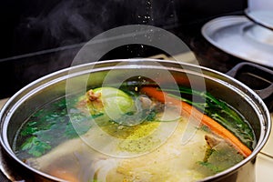 Pouring seasoning into boiling chicken broth with vegetables in steel pot