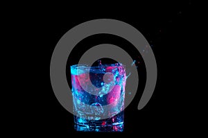 Pouring from the side and splashing in a rocks glass under blue and red lights isolated on a black background