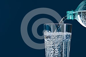 Pouring soda water from bottle into glass on blue background, closeup. Space for text